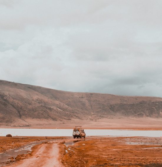 a truck driving down a dirt road next to a body of water